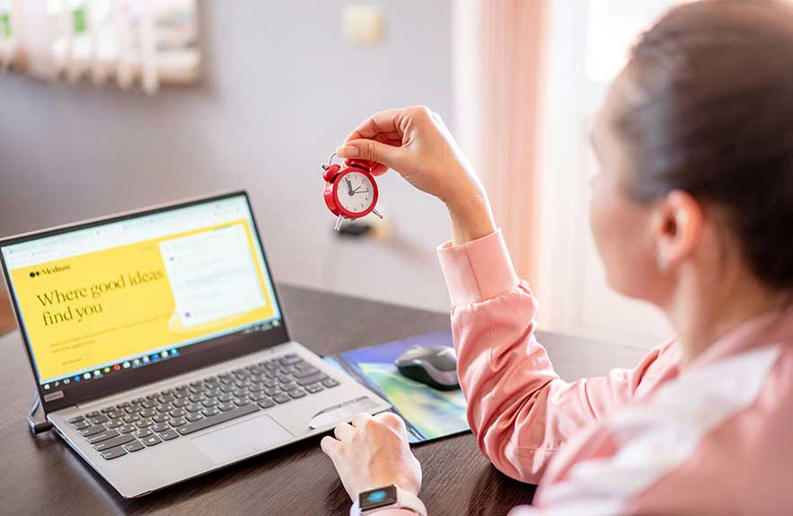 Woman using time management tools while holding a mini clock at desk