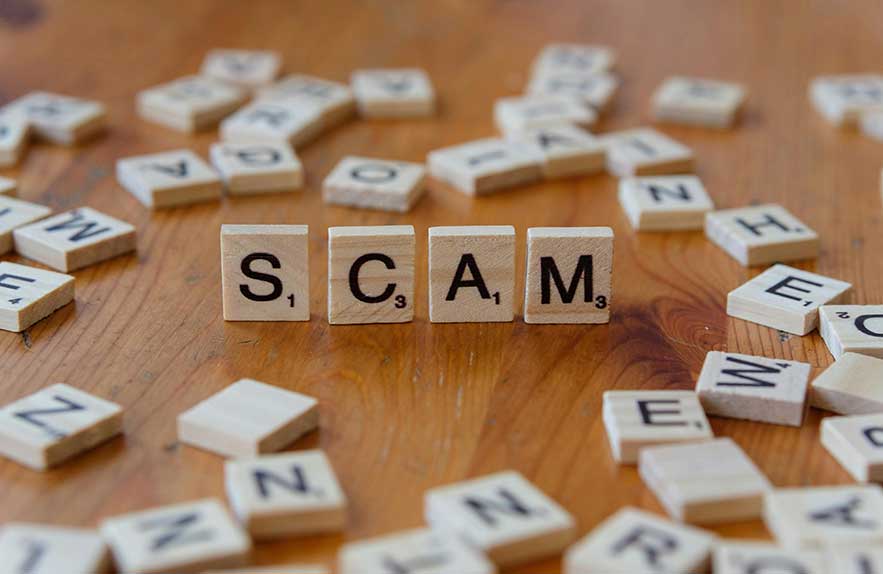 Wooden letter tiles spelling “SCAM” surrounded by jumbled letters, representing the rise of common online scams and cyber threats in 2025