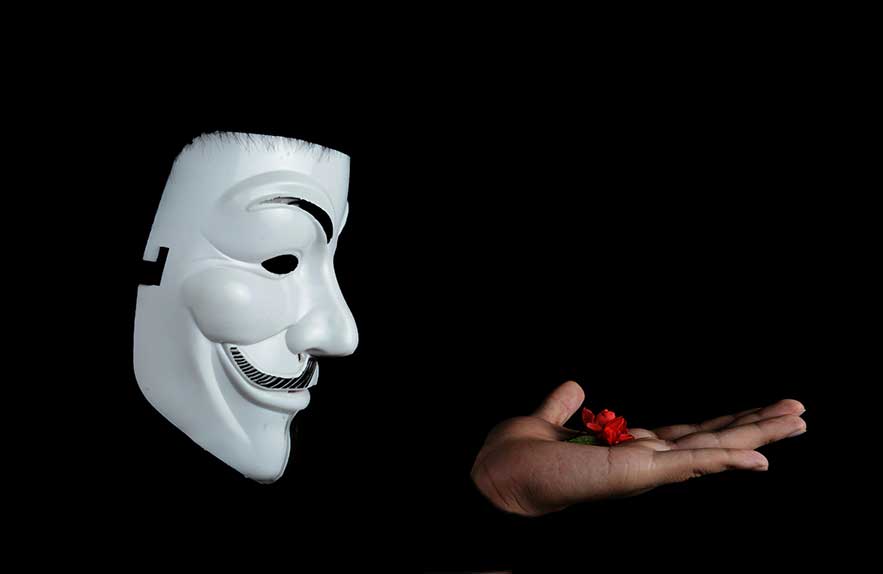 Social engineering concept with anonymous mask and deceptive hand offering a flower on dark background